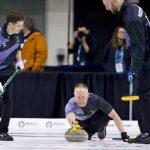 Curling skip releasing a stone during a match with focused teammates in the background